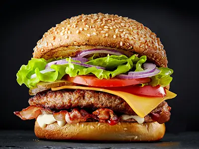 Bacon cheeseburger with lettuce, tomato, and onion on a sesame bun